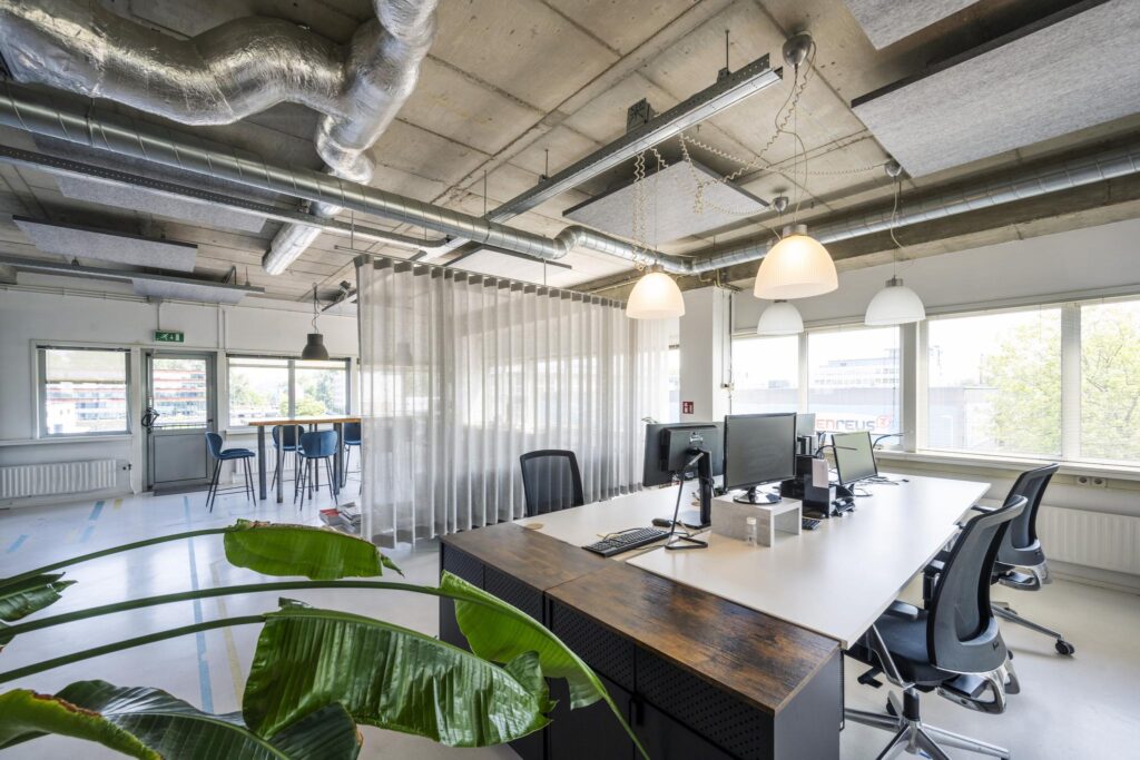 Modern kantoorinterieur aan de Anthony Fokkerweg met open werkplekken, grote ramen en industriële plafondafwerking.